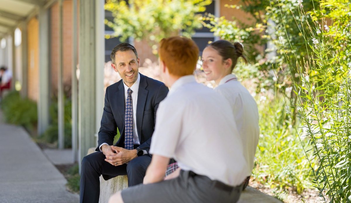 A teacher interacting with two students in an outdoor setting.