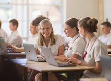 A teacher interacting with students using their laptops in a classroom.